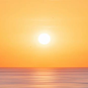 Golden sunrise warms the tranquil sea horizon in orange and pink hues.