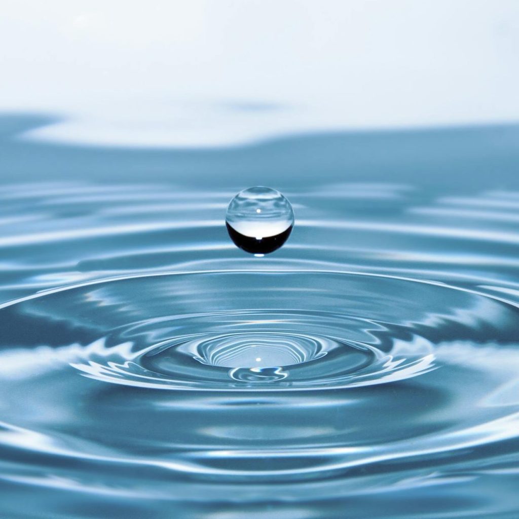 Lone droplet embracing infinite rippling vastness below