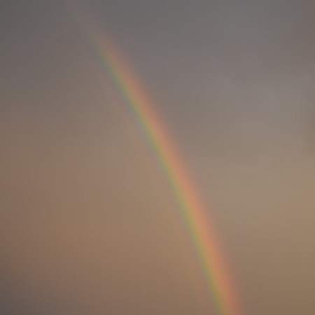 Rainbow's origin piercing cloudy sky, touching barren desolate earth